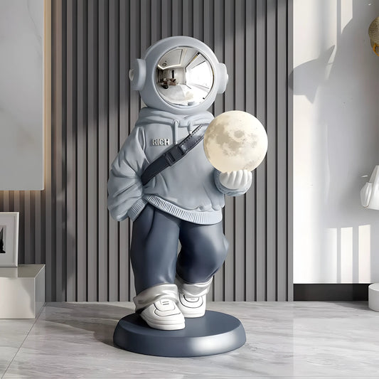 Decorative figure of an astronaut holding a moon, standing on a wooden floor with a striped wall in the background.