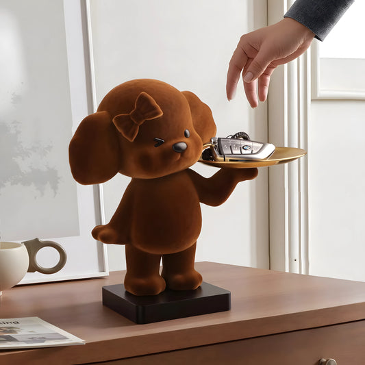 A brown cartoon dog-shaped desk organizer holding a gold tray with keys, placed on a wooden table with a hand reaching toward the tray.