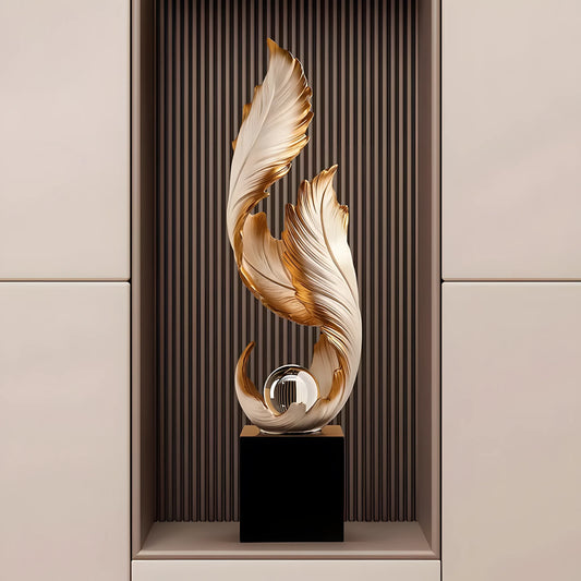 A modern abstract decorative sculpture featuring layered, flowing leaf-like forms in cream and metallic gold, mounted on a black rectangular base with a reflective glass orb at the center, displayed against a vertical ribbed brown panel and beige side panels.