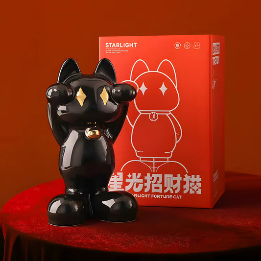 A glossy black cat figurine with gold diamond-shaped eyes and a gold bell stands in front of its red packaging box. The box features a white line drawing of the cat and the text 'STARLIGHT' and 'FORTUNE CAT'.