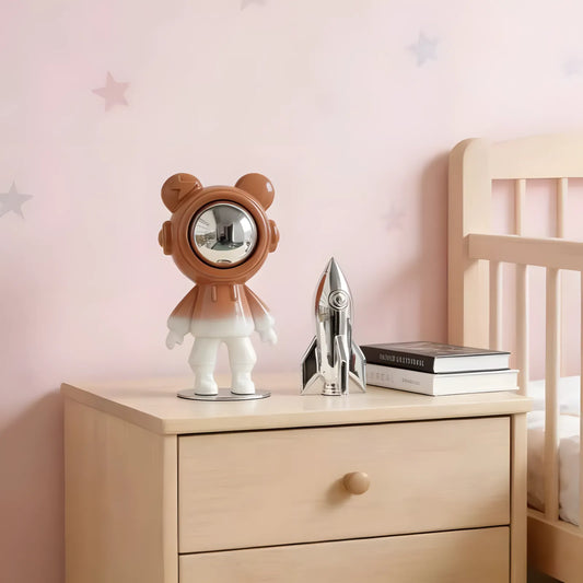 Modern glossy orange astronaut bear sculpture with silver visor on a nightstand next to a toy rocket