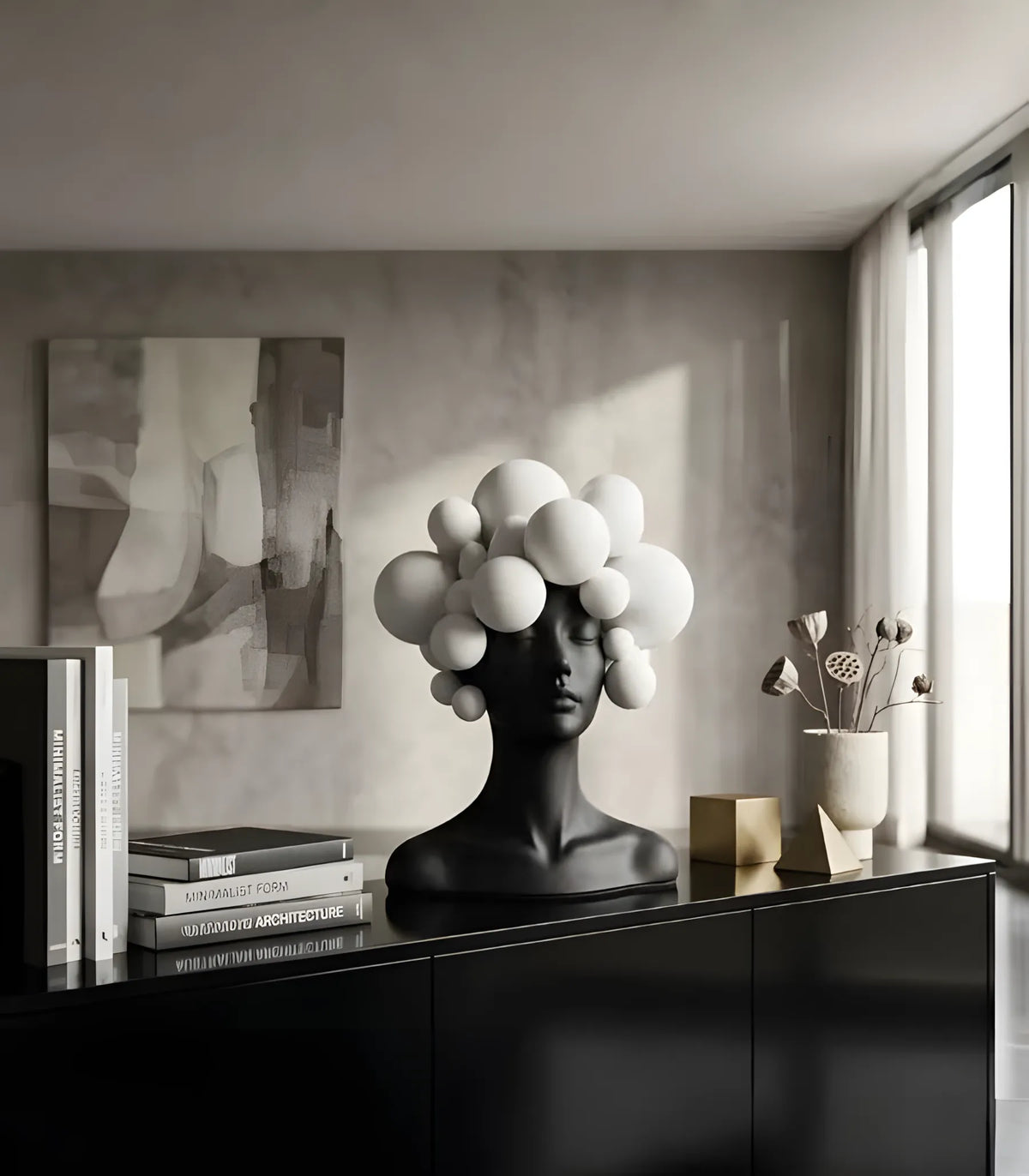 A black sculptural bust with a cluster of white spherical shapes emerging from the head, displayed on a glossy black cabinet in a modern interior room with books, a vase, and a window.