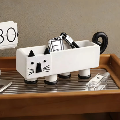 A white ceramic cat-shaped desk organizer with black accents, holding a silver car key fob, displayed on a wooden tray with a beige textured background.