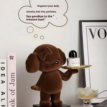 A brown plush dog figurine holding a small tray with a perfume bottle, displayed on a tabletop with decorative books, a framed print, and a thought bubble graphic on a white wall.