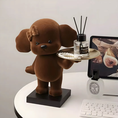 A brown plush puppy figurine holding a tray with a diffuser and pearls, styled on a white desk next to a computer monitor and keyboard.
