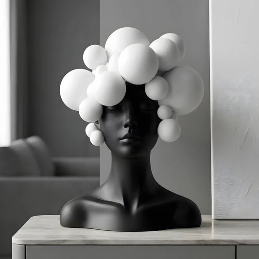 Abstract black female bust sculpture with large white bubble-like forms emerging from the head, displayed on a light marble surface against a gray interior background.