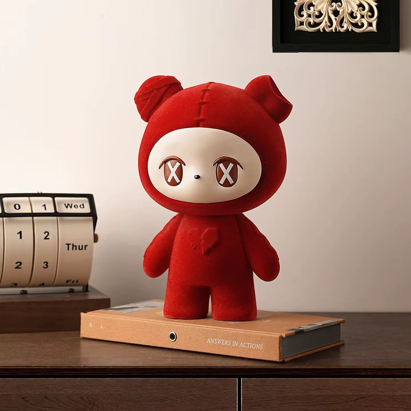 Red plush toy with a neutral expression on a wooden surface next to a calendar.