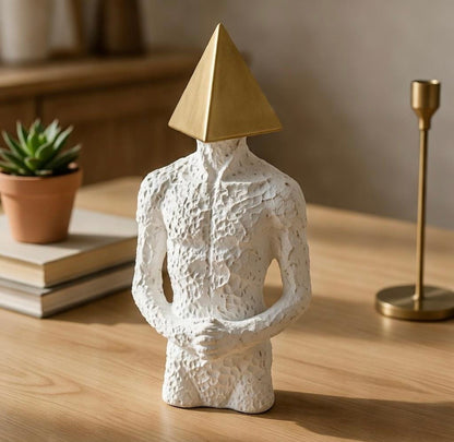 Decorative sculpture with a textured white body and gold pyramid on head, placed on a wooden surface.