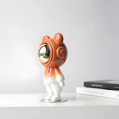 Modern glossy orange astronaut bear sculpture with silver visor on a nightstand next to a toy rocket