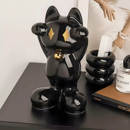 A glossy black bear-shaped tissue box cover or decorative holder with gold diamond accents on the eyes and a gold bell at the belly, shown on a dark tabletop beside other home decor items.