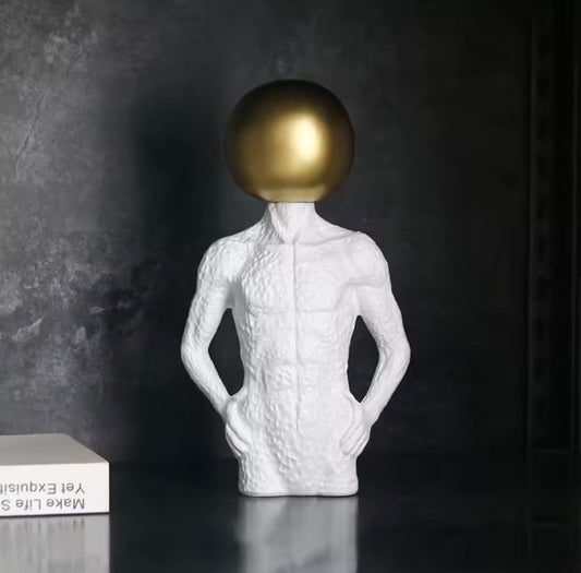 White textured sculpture with a gold sphere for a head on a dark background