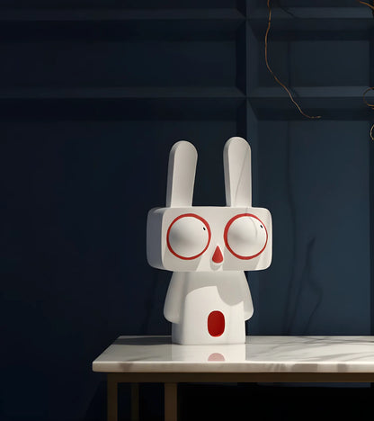 Large white big-eyed bunny art sculpture displayed on a sleek marble tabletop against a moody dark blue accent wall