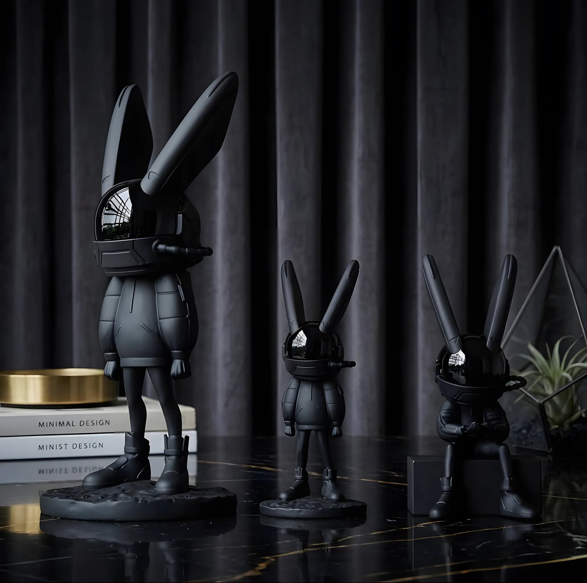 Three distinct matte black astronaut rabbit art figurines shown together on a polished marble surface against a dark pleated curtain background