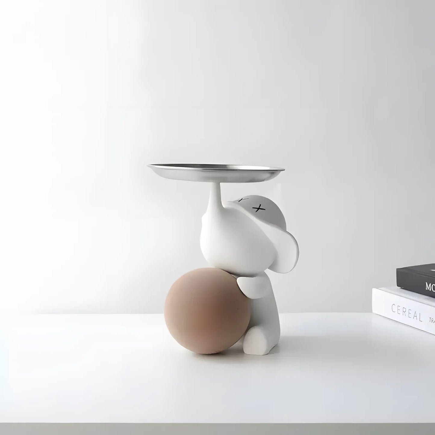 Side view of the modern white elephant figurine with a beige brown sphere on a clean white tabletop surface