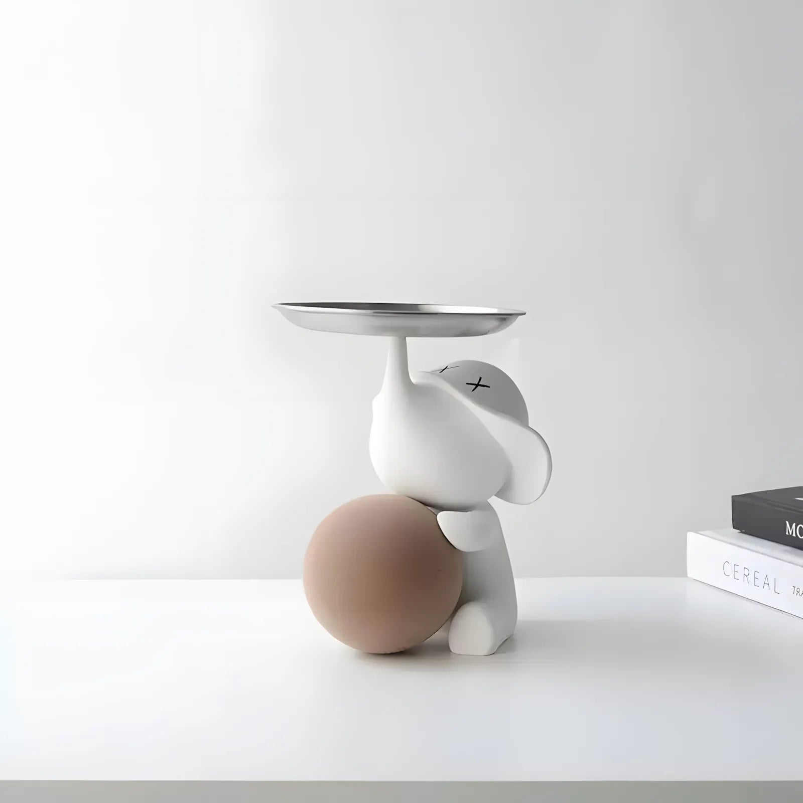 Side view of the modern white elephant figurine with a beige brown sphere on a clean white tabletop surface