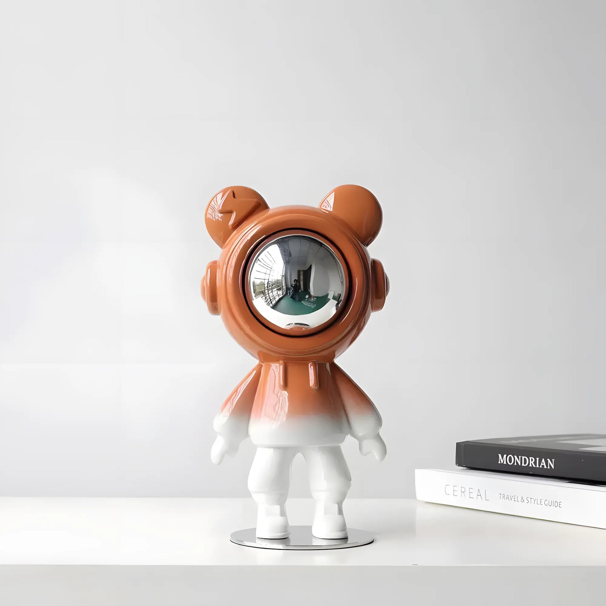 Modern glossy orange astronaut bear sculpture with silver visor on a nightstand next to a toy rocket