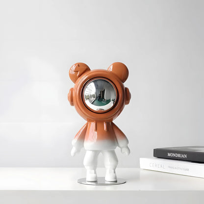 Modern glossy orange astronaut bear sculpture with silver visor on a nightstand next to a toy rocket