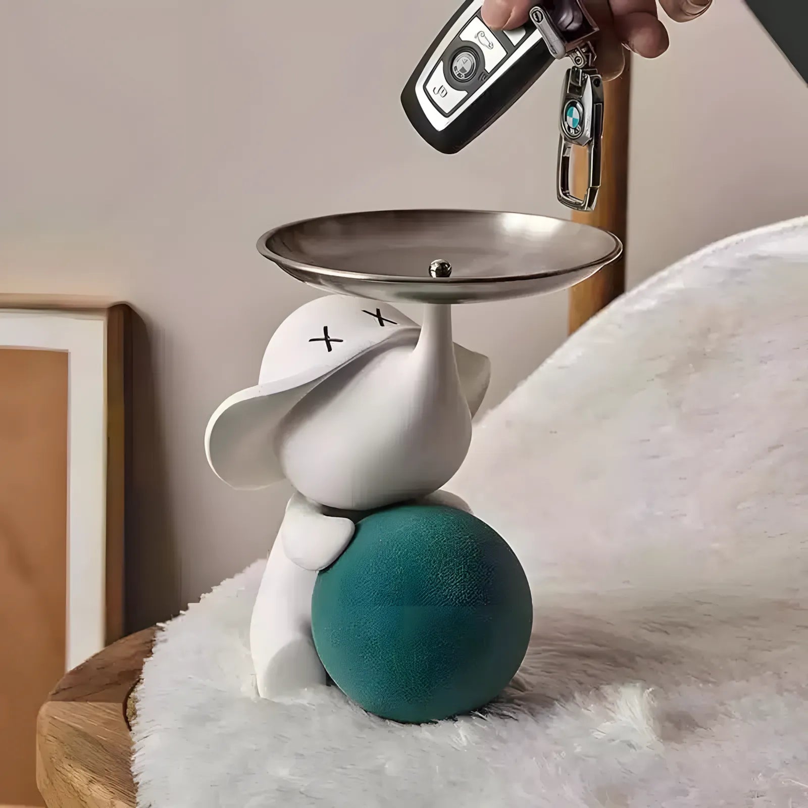 Hand dropping car keys into the silver tray of a modern white elephant pop art sculpture on a wooden table