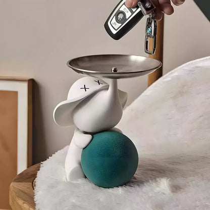 Hand dropping car keys into the silver tray of a modern white elephant pop art sculpture on a wooden table