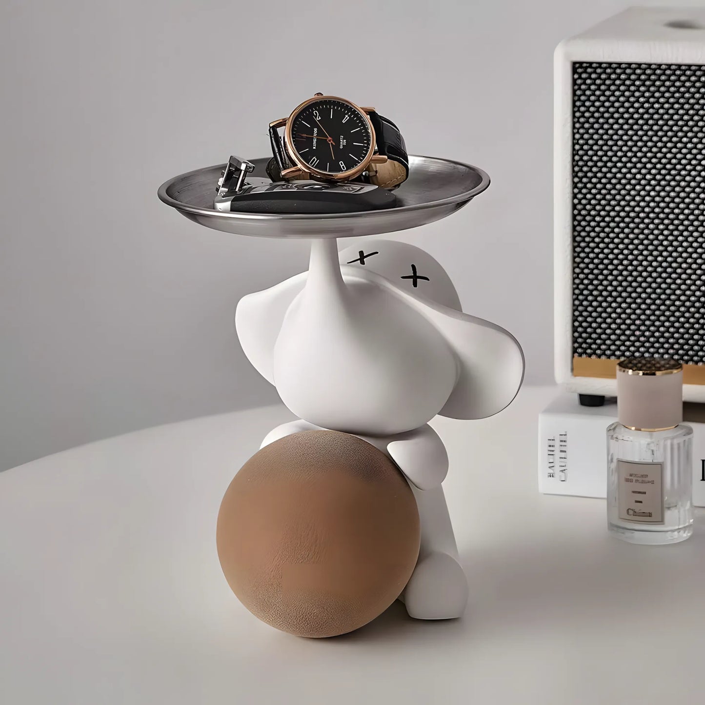 Front view of the contemporary matte white elephant organizer statuette holding a warm beige ball next to a perfume bottle