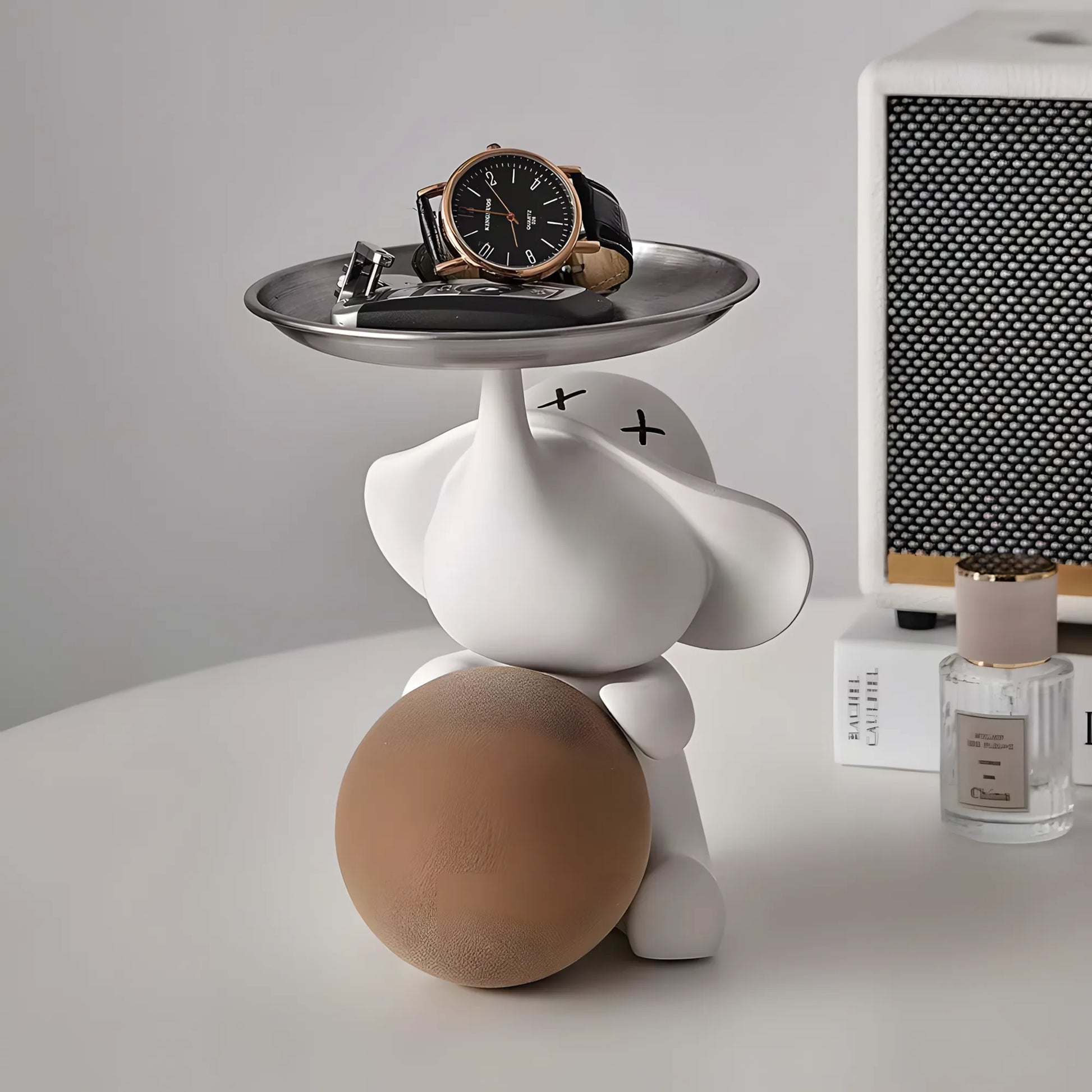 Front view of the contemporary matte white elephant organizer statuette holding a warm beige ball next to a perfume bottle