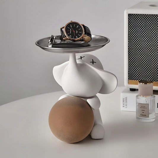 Front view of the contemporary matte white elephant organizer statuette holding a warm beige ball next to a perfume bottle