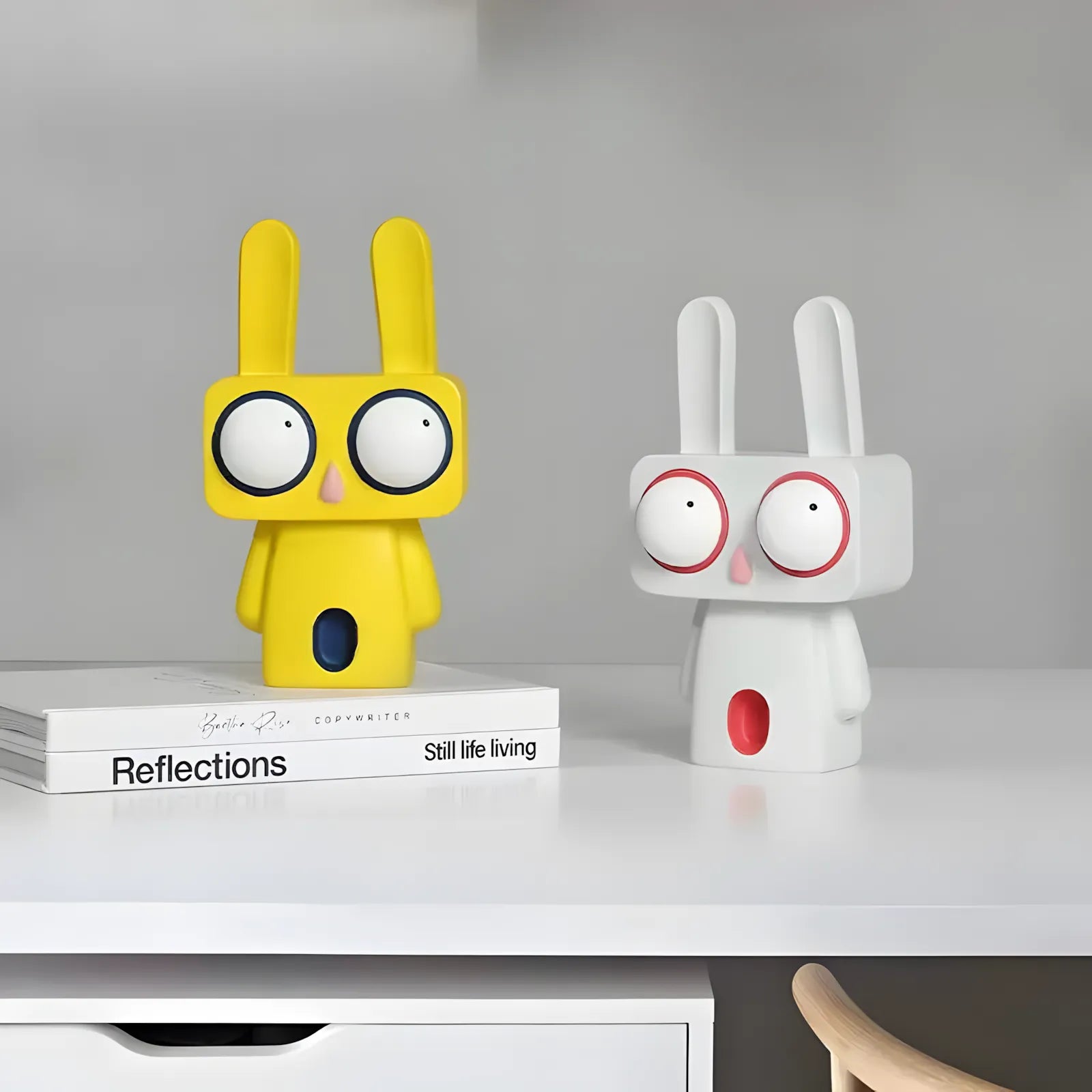Two colorful rabbit-shaped figurines on a shelf with a book titled 'Reflections'.